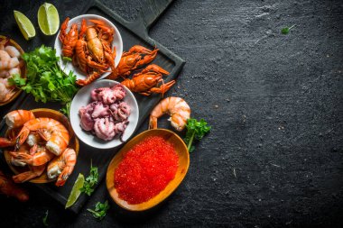 Havyar ve deniz ürünleri otlar ve kireç dilimleri ile bir kesme Kurulu üzerinde. Siyah rustik arka plan üzerinde