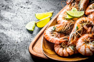 Kesme tahtasında tabakta pişmiş karidesler. Siyah rustik arka plan üzerinde