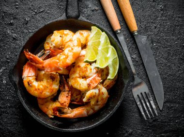 Limon dilimleri ile bir tavada taze kızarmış karides. Siyah rustik arka plan üzerinde