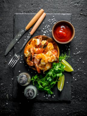 Baharat, domates sosu ve otlar ile bir taş tahta üzerinde Karides. Siyah rustik arka plan üzerinde