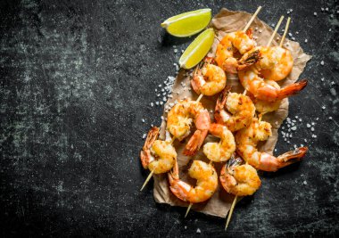 Karidesler şişlerde kireç dilimleriile kızartılır. Koyu rustik arka plan üzerinde