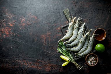 Limon, biberiye ve baharatile kesme Tahtası üzerinde çiğ karides. Koyu rustik arka plan üzerinde