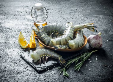 Taş bir tahtanın üzerinde limon dilimleriyle çiğ karides. Siyah kırsal arkaplanda