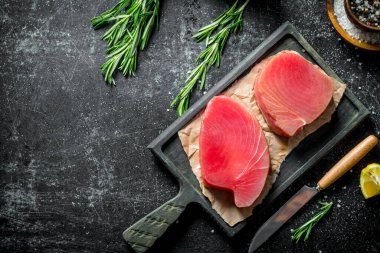 Baharat ve biberiye ile kesme Tahtası üzerinde ham ton balığı fileto. Koyu rustik arka plan üzerinde