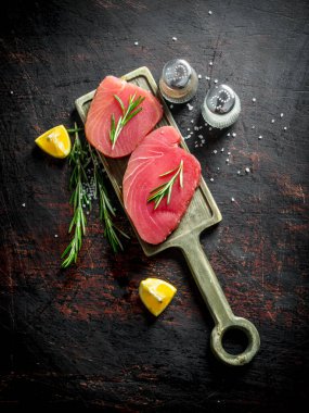 Baharat, limon ve biberiye ile kesme Tahtası üzerinde taze çiğ ton balığı parçaları. Koyu rustik arka plan üzerinde