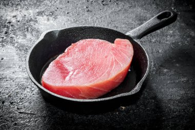 Tavada taze çiğ ton balığı bifteği. Siyah rustik arka plan üzerinde