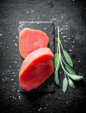 Salvia bir sprig ile bir taş Tahta üzerinde taze çiğ ton balığı. Siyah rustik arka plan üzerinde