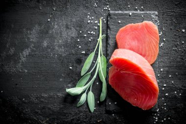 Baharat, salvia ve limon dilimleri ile bir taş Tahta üzerinde Çiğ ton balığı biftek. Siyah rustik arka plan üzerinde