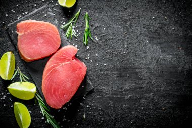 Limon ve biberiye ile taze çiğ ton balığı biftek. Siyah rustik arka plan üzerinde