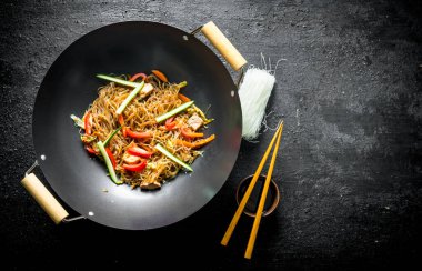 Bir kase ve çubukları ile soya sosu ile Pişmiş Çin erişte selofan wok. Siyah rustik arka plan üzerinde