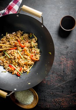Bir tabak ve soya sosu üzerinde çiğ pirinç ile bir wok tavada sebze ile taze pişmiş pirinç. Koyu rustik arka plan üzerinde