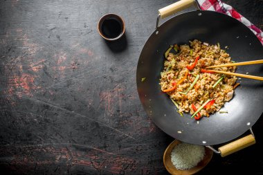 Bir tabak ve soya sosu üzerinde çiğ pirinç ile bir wok tavada sebze ile taze pişmiş pirinç. Koyu rustik arka plan üzerinde