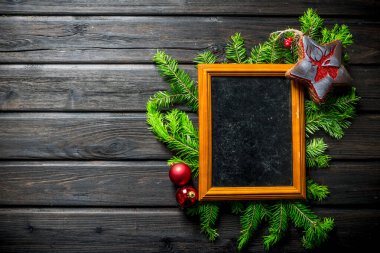 Köknar dalları ve süslemeleri olan boş bir Noel fotoğrafı çerçevesi. Koyu bir ahşap arka planda