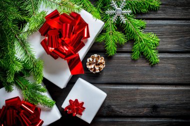 Kırmızı fiyonklu Noel kutuları, köknar dalları ve bir koni. Koyu bir ahşap arka planda