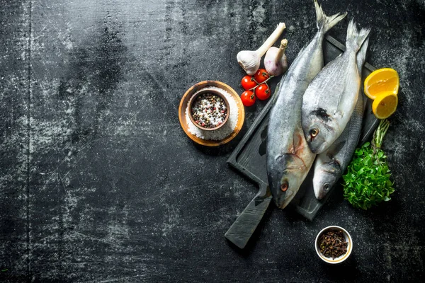 stock image Fresh fish on a cutting Board with herbs, spices, tomatoes and garlic. On dark rustic background