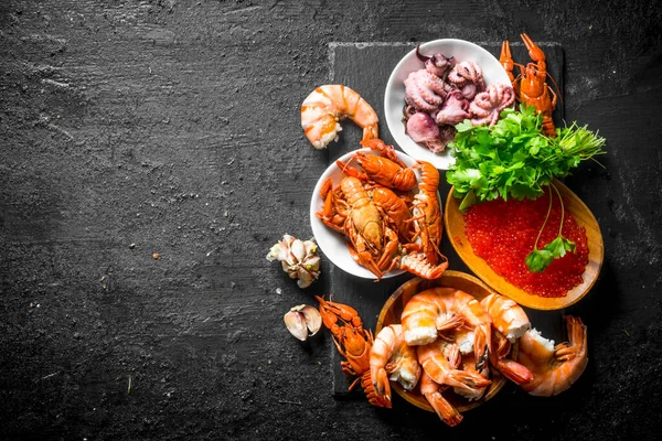 stock image Seafood. Shrimp, crayfish, octopus and caviar with parsley and garlic cloves. On black rustic background