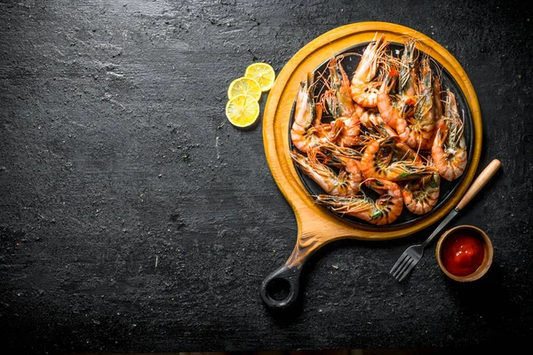 stock image Grilled shrimps on a cutting Board with tomato sauce and sliced lemon. On black rustic background