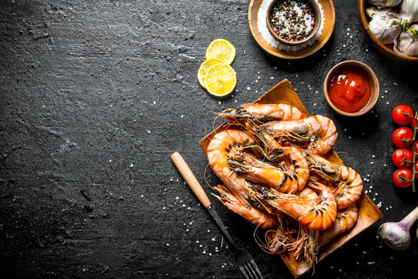 stock image Delicious shrimps with spices, tomato sauce and lemon slices. On black rustic background