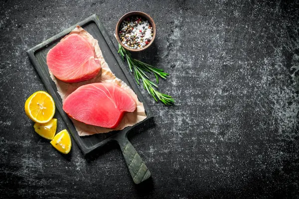 stock image Fresh raw tuna steak on a cutting Board with lemon slices, rosemary and spices. On dark rustic background