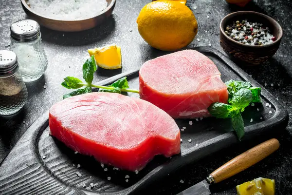 Otlar ve limon dilimleri ile bir kesme Tahtası üzerinde ham ton balığı parçaları. Koyu rustik arka plan üzerinde
