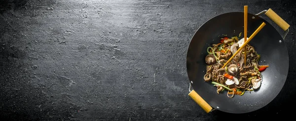 stock image Chinese noodles wok soba in a frying pan with chopsticks. On black rustic background