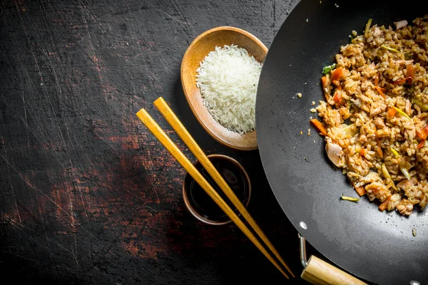 stock image Chinese wok. Cooked rice in a wok pan and uncooked rice on a plate. On dark rustic background