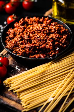 Çeri domatesleri ve kuru makarnayla kesilmiş bolonez sosu. Karanlık bir arka plana karşı. Yüksek kalite fotoğraf