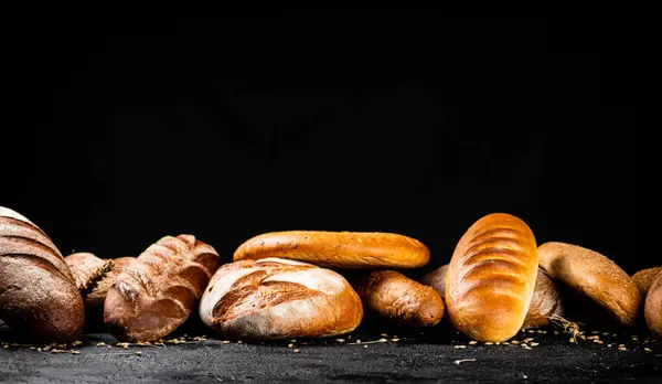 stock image Different types of fresh bread on the table. On a black background. High quality photo