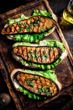 Kesme tahtasının üzerinde ızgara patlıcanlı güzel kokulu bir sandviç. Karanlık bir arka plana karşı. Yüksek kalite fotoğraf