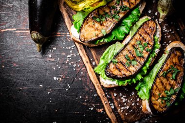 Kesme tahtasının üzerinde ızgara patlıcanlı güzel kokulu bir sandviç. Karanlık bir arka plana karşı. Yüksek kalite fotoğraf