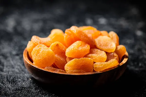 stock image Delicious dried apricots in a wooden plate. On a black background. High quality photo