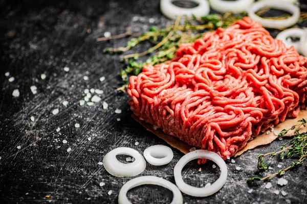 stock image A piece of fresh minced meat on paper with onion rings and thyme. On a black background. High quality photo