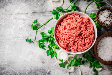 Maydanoz ve soğan halkaları olan bir masada kasede kıyma. Gri bir arka planda. Yüksek kalite fotoğraf