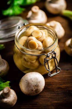 Masanın üzerinde mantar turşusu olan küçük cam bir kavanoz. Ahşap bir arka planda. Yüksek kalite fotoğraf