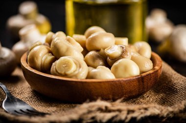 Çuval bezi üzerinde ahşap tabak ve mantar turşusu. Karanlık bir arka plana karşı. Yüksek kalite fotoğraf