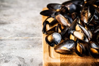 Tahta kesme tahtasının üzerinde haşlanmış midyeler. Gri bir arka planda. Yüksek kalite fotoğraf