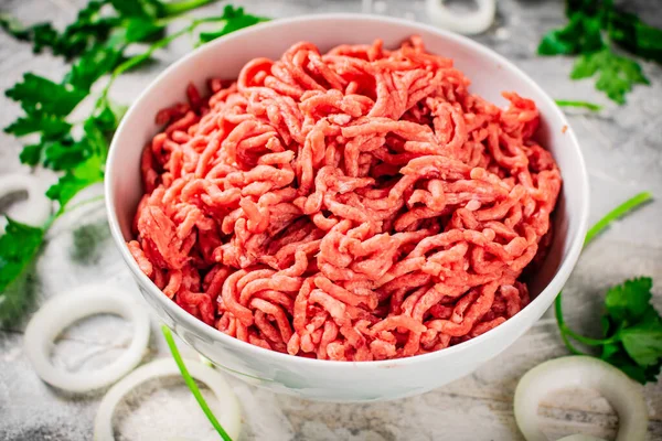 stock image Minced meat in a bowl on a table with parsley and onion rings. On a gray background. High quality photo