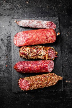 Taş bir tahtanın üzerinde farklı salam parçaları. Siyah bir arka planda. Yüksek kalite fotoğraf