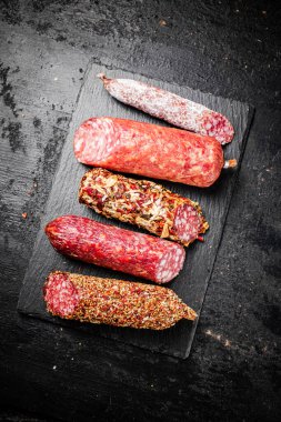 Taş bir tahtanın üzerinde farklı salam parçaları. Siyah bir arka planda. Yüksek kalite fotoğraf