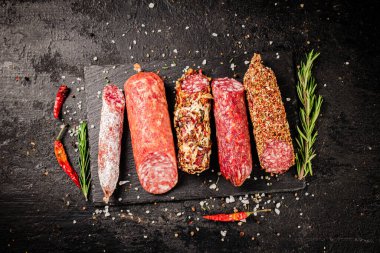 Biberiyeli taş bir tahtanın üzerinde lezzetli bir salam sosisi çeşidi. Siyah bir arka planda. Yüksek kalite fotoğraf