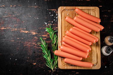 Sosisler ahşap bir kesme tahtasında biberiye filizi ile kaynatılmış. Karanlık bir arka plana karşı. Yüksek kalite fotoğraf
