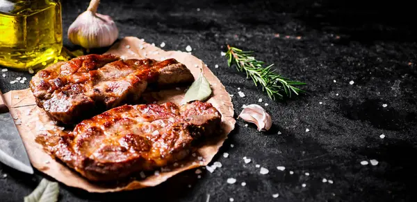 stock image Grilled pork steak on paper on the table. On a black background. High quality photo