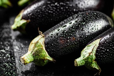 Fresh ripe eggplant with droplets of water on a stone board. On a black background. High quality photo