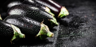 Fresh ripe eggplant with droplets of water on a stone board. On a black background. High quality photo