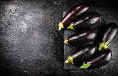 Fresh ripe eggplant with droplets of water on a stone board. On a black background. High quality photo