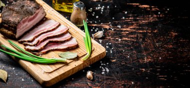 Pieces of pork lard on a cutting board with green onions and bay leaves. Against a dark background. High quality photo