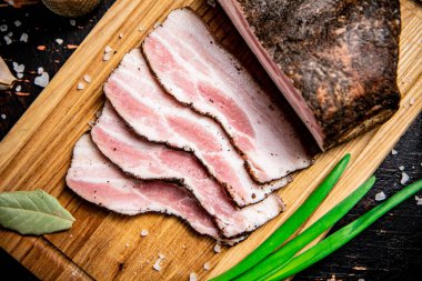 Pieces of pork lard on a cutting board with green onions and bay leaves. Against a dark background. High quality photo