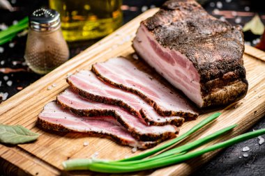 Pieces of pork lard on a cutting board with green onions and bay leaves. Against a dark background. High quality photo