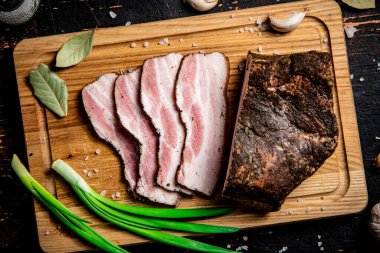 Pieces of pork lard on a cutting board with green onions and bay leaves. Against a dark background. High quality photo
