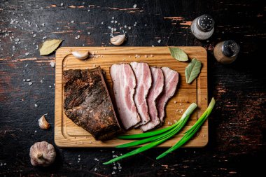 Pieces of pork lard on a cutting board with green onions and bay leaves. Against a dark background. High quality photo